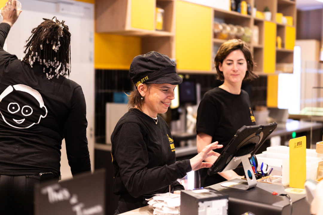 Charlotte, équipière au Café Joyeux Crystal Park, accompagnée à la caisse par Anne-Laure, encadrante